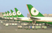 Row of eight aircraft tails in identical livery, lined at airport terminal, surrounded by cargo and equipment.