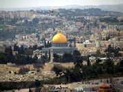 A city scene. Many of the buildings look ancient. In the centre, there is a large building topped by a golden dome. In the background, there are modern-looking high-rise buildings.