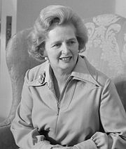 A black and white photo of Thatcher in a light coloured raincoat, sitting in a comfortable chair.