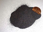 A small heap of uniform black grains smaller than 1mm diameter with a US 1 Cent sticking out of the heap.