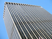 Street view of top half of skyscraper against the sky; its outside is dominated by vertical black and white lines