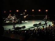 A colorful, round stage inside an arena, with all four of the band members performing their instruments.