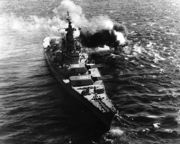 A large ship resting on the ocean, with smoke visible from the back of the vessel.