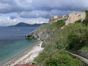 Photo of a coastline with the sea, greyish cliffs, vegetation and beige buildings