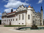  Large rectangular building of pale stonework, multiple rectangular windows and ornamental features at the roof level