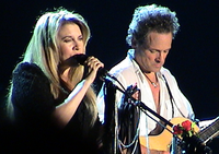 A blonde, female singer and a male acoustic guitarist are performing together in concert.