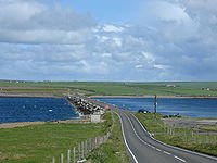 The causeway, made from many concrete blocks, carries a two-lane road between the islands. The sea is rough on one side of the barrier but calm on the other.