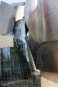  Outside view of a several storey building with smooth irregular undulating walls. The largest part is coated with gray metal or made from glass