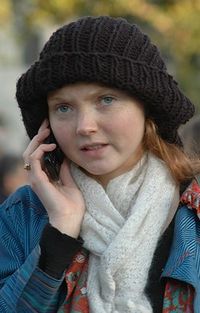 the head and shoulders of Cole outside on a mobile phone wearing a black beret, blue coat and white scarf