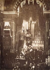 Looking down upon an assembly in a large, vaulted cathedral with a figure sitting on a large, canopied throne to the left of an altar