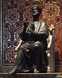  Peter is shown as a bearded man in draped garment like a toga. He is seated on a chair made of marble, and has his right hand raised in a gesture of blessing while in his left hand he holds two large keys. Behind the statue, the wall is patterned in mosaic to resemble red and gold brocade cloth.