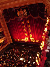 interior of a traditional nineteenth century theatre, with red plush curtains and much gilt decoration