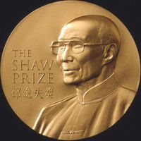 A gold circular medal with a depiction of an elderly man with glasses wearing a jacket buttoned to the neck; the English words "The Shaw Prize" and Chinese characters "邵逸夫獎" engraved on it