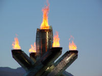 four pillars with flame at their tops surrounding a single fifth pillar in the middle, also with flame at the top.  The background is sky with mountain.