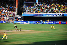 Cricketers in a game in front of nearly-full stands.