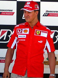 The head and torso of a man in his 30's, wearing a red cap and red top. His clothing features various logos, as does the black and white chequred wall behind him.