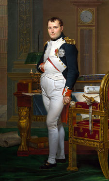 Full length portrait of Napoleon in his forties, in high-ranking white and dark blue military dress uniform. He stands amid rich 18th-century furniture laden with papers, and gazes at the viewer. His hair is Brutus style, cropped close but with a short fringe in front, and his right hand is tucked in his waistcoat.