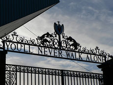 Design of the top of a set of gates, with the sky visible. The inscription on the gates reads "You'll Never Walk Alone".