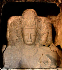 A brownish stone three-headed statue carved with ornaments