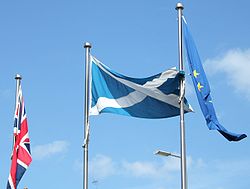 Union Flag, Scottish Flag and EU Flag on poles against a blue sky.