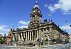 An impressive free-standing stone-built civic building on a sloping site with steps up to a colonnade.  Above the parapet is a square clock-tower, also colonnaded, with an elongated lead-covered dome with concave sides and a cupola on top.