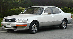 Front quarter view of sedan parked on a street in front of hedges.