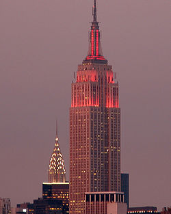 Partial view of a 100-story building with several setbacks; the building tapers into a large circular spire near its 90th floor and is topped by a large antenna. Pink lights light up the building's midsecction and spire.