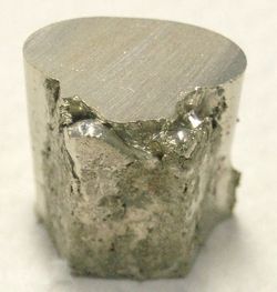 A pitted and lumpy piece of silvery metal, with the top surface cut flat