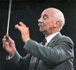 head and shoulders of an elderly man with thinning white hair and moustache; his arms are raised; there is a conductor's baton in his right hand