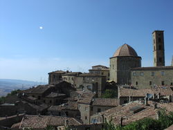 Photo of an Italian town on a hillside, with a six-sided tower and tiled roof tops.