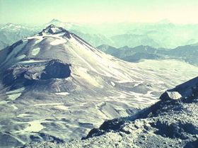 A conical mountain with patches of snow and ice lies behind a deep crater.