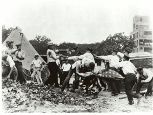  Police with batons confront demonstrators armed with bricks and clubs. A policeman and a demonstrator wrestle over a U.S. flag.