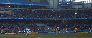 A football match in progress featuring a team in blue and a team in yellow. In the background, stands are visible. They are well occupied