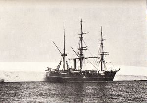  Three-masted ship with sails furled, lying next to a shelf of ice.