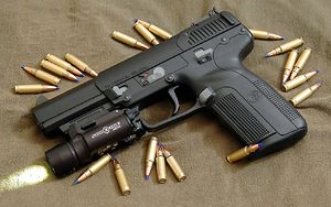 Photo of the Five-seven USG pistol equipped with a tactical light and surrounded by 5.7x28mm SS197SR cartridges