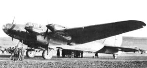 Three-quarters view of a large four-engined parked aircraft with a conventional undercarriage with a group of people clustered in the left foreground and another on the other side of the fuselage in the background