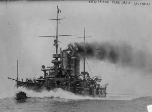 A small grey battleship traveling at full speed with smoke coming out of its two round funnels.