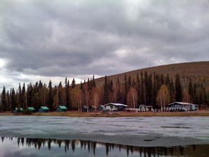 Scattered cabins are seen behind a lake with ice floating on its surface