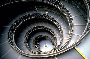 The staircase has two parts, a double helix, and is of shallow incline, being a stepped ramp rather than a true staircase. It is encircles the outer wall of a stair well of approximately fifteen meters wide and with a clear space at the centre. The balustrade around the ramp is of ornately worked metal.