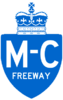 A Macdonald–Cartier Freeway reassurance marker. It is the same shape as the 401 marker, except blue with white text as opposed to white on black text. In place of the number 401 is M-C, and below that FREEWAY. There is no ONTARIO on this marker.