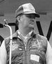 A black and white image of a Lynch wearing a baseball hat and a jacket with his medal of honor visible around his neck.