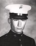 Head of a young white man wearing a white peaked cap with black visor and a dark military jacket.