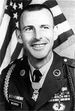 A black and white image of Morris from the chest up in his military dress uniform with ribbons. He has no hat and there is an American flag in the background.