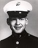 Head of a young white man with a big smile, wearing a white peaked cap with black visor and a dark military jacket.