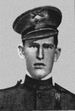 Face of a young man in military uniform. He has a stern expression and his hat, a peaked cap, is slightly cocked.