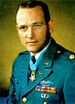 Head and shoulders of a white man with short brown hair, wearing a green military jacket with a star-shaped medal hanging from a blue ribbon around his neck.