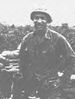 A black and white image showing Hector from the waist up in his military combat uniform with kevlar helmet. His hands are on his hips and he is smiling at the camera.