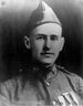 Head of a young man in military uniform with a garrison cap and round "US" pins on either side of his high, stiff collar.