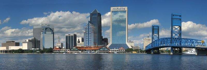 A city with several tall buildings and a bridge spanning the river, running in front of the buildings