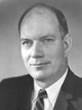 Black and white photo of a balding man in a suit and striped tie